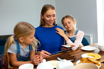 Happy mother having breakfast with daughters at home