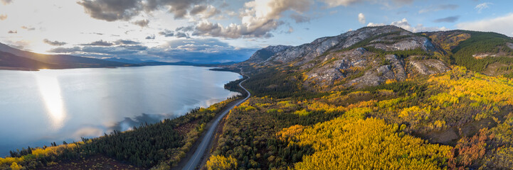 Stunning fall autumn landscape in northern Canada, Yukon Territory. Taken by drone on the side of a lake with mountains and road. 