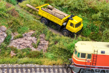 Yellow truck on model train railroad layout in H0 scale with wood near locomotive