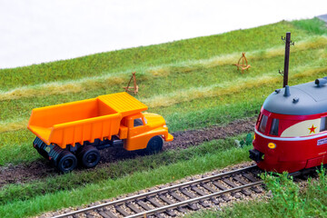 Orange truck on model train layout pass by passenger train