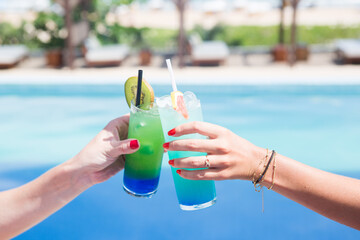 toast with two blue drinks with a pool in the background