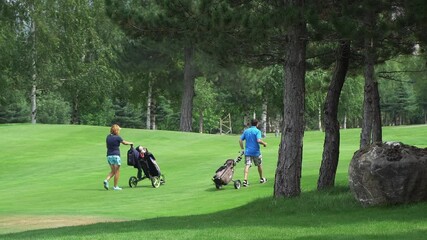 Players  golfers walking on perfect golf course at summer day pushing an equipment carts, slow motion