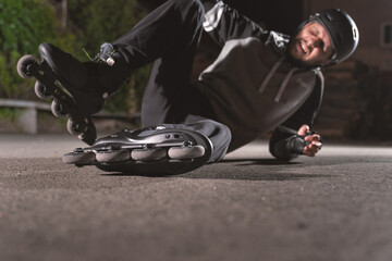 Selective focus inline roller skates caucasian man fallen on the asphalt ground while driving at...