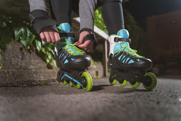 Hands of unknown girl woman tie laces inline roller skates at night