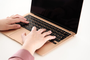 Woman hands using a gold laptop, incredibly thin, light and perfectly portable notebook open with blank black screen on a white wooden table.