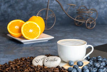 a cup of morning coffee on a plain background, coffee beans, oranges and blueberries