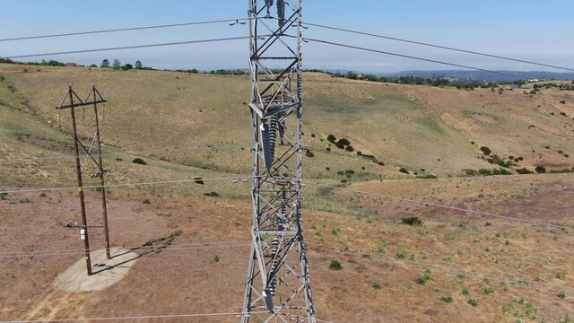 Aerial view of electricity transmission pylon in dry valley landscape. High voltage electricity distribution, California