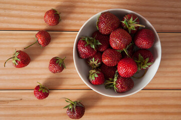 Fresh juicy sweet strawberries in a bowl and scattered close-up on a wooden background. Selective focus.