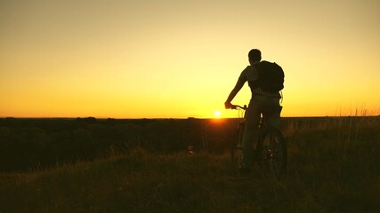 Hiker healthy young man rides a bicycle to edge of the hill, enjoying nature and sun. free traveler travels with a bicycle at sunset. concept of adventure and travel. lonely cyclist resting in park.