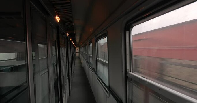Interior of a passenger train with empty corridor and cabins, another freight train passing by