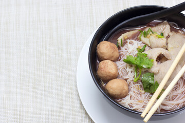 Waterfall noodles, put pork and meatballs in a black cup with a white tray on the fabric surface