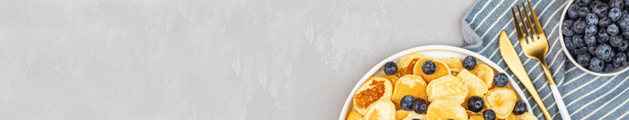 Trendy home breakfast with tiny pancakes and blueberry on gray concrete background. Flat lay, top view, overhead, mockup, template, copy space. View from above. High quality photo