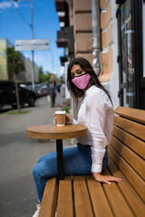 Woman in a medical mask drinks coffee on the street