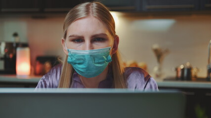 Medium shot of computer monitor and business woman in medical mask reading something on it. She working at home on quarantine.