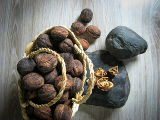 The whole walnuts are  into a wicker basket next to Walnuts broken on the stone on wooden table....