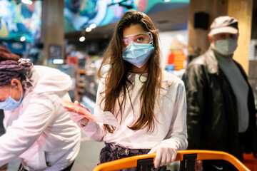 Fototapeta na wymiar Woman with the surgical mask and the gloves is shopping in the supermarket