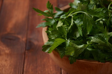 Parsley bunch in a bowl on wood table background. Fresh parsley on wooden background. Organic parsley closeup on rustic board, vegetarian food overhead. 