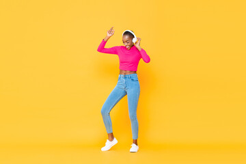 Fototapeta na wymiar Happy African American woman wearing headphones listening to music and dancing on colorful yellow isolated background