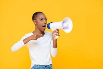 African American woman shouting on megaphone and pointing hand isolated on yellow background