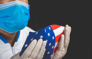 Medical personnel in a white long sleeve shirt wearing medical masks holding the American flag on black background