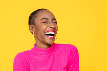 Happy optimistic African American woman in colorful pink clothes laughing isolated on yellow background - obrazy, fototapety, plakaty