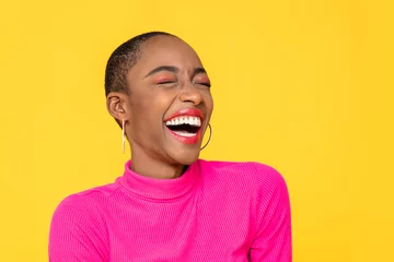Fotobehang Happy optimistic African American woman in colorful pink clothes laughing isolated on yellow background © Atstock Productions
