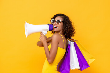 Happy beautiful woman with shopping bags and megaphone on isolated colorful yellow background for...