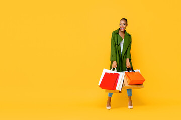 Fashionable African American woman with colorful shopping bags  isolated on yellow background