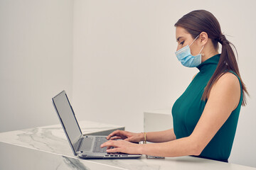 Mujer ejecutiva revisando correos en la computadora, con mascarilla debido a la nueva normalidad...