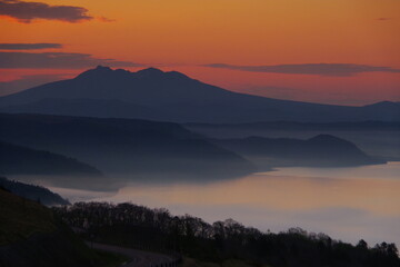 遠くの山のシルエットと朝靄の湖。峠からの風景。美幌峠、北海道、日本。