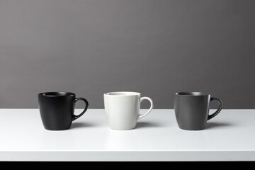 Three black, grey and white isolated tea cups on the table. Horizontal table and construction lines. Copy space for editing. Modern monochrome wallpaper 