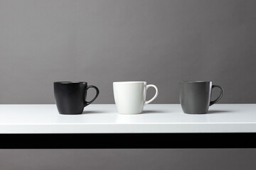Three black, grey and white isolated tea cups on the table. Horizontal table and construction lines. Copy space for editing. Modern monochrome wallpaper 