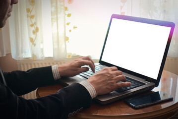 Man typing and browsing with laptop on a table at home, blank screen copy space