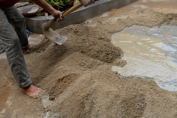 Indian labour mixing cement and water manually on floor using a shovel. Stock image.