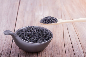 Wooden spoon scoop black sesame seeds in a cup placed on a wooden table