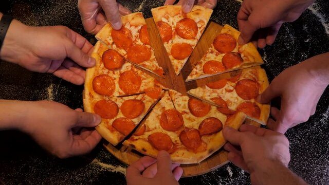 Hands are taking slices of pepperoni pizza away from the wooden board. Black table background.