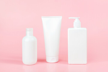 Obraz na płótnie Canvas Set of care cosmetic for skin, body or hair. Three white blank cosmetics bottles, tube on pink background. Spa Cosmetic Beauty Concept. Front view Mockup