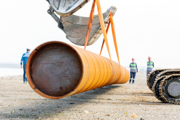 Excavators are lifting a large steel pipe pile and occupational safety specialists control the...