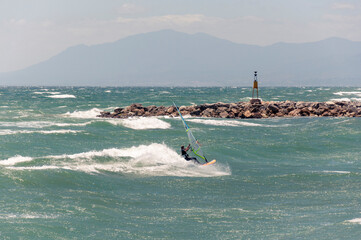 Windsurfer riding waves at sunny windy day, along a stone pier, against the backdrop of the...
