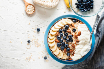 Breakfast, oatmeal with blueberry, banana almond and yogurt on a bowl in the morning.