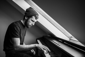 Musician and composer in a hat plays piano, black and white, The pianist performs a musical work on...