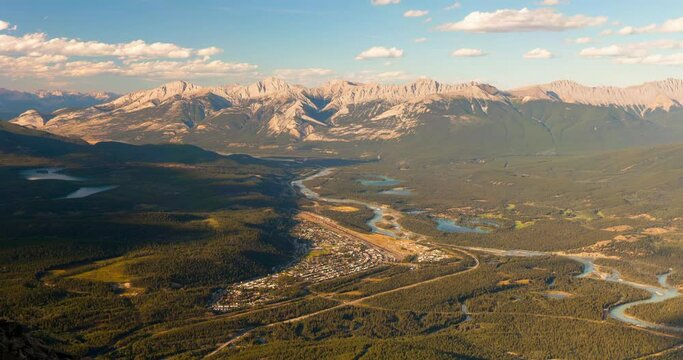 Lockdown time lapse shot of city by river near mountains against sky on sunny day - Jasper National Park, Canada