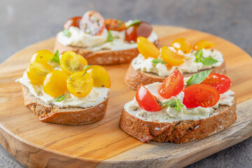 Delicious crusty bread slices with cream cheese and different tomato cherry  garnished with fresh basil leaves on the table .Appetizer bruschetta or snack