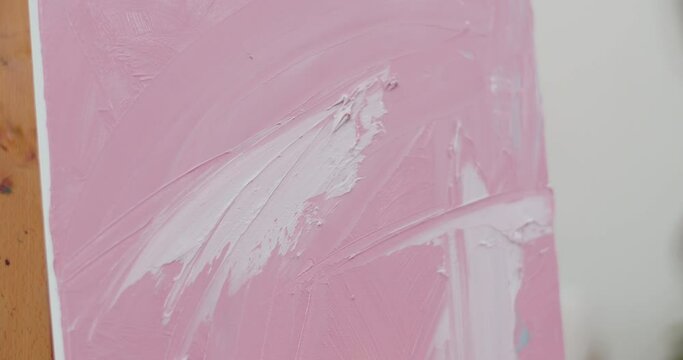 Close up view of female artist hand drawing acrylic pink and white colors on warm light.Painting picture on molbert with spatula and acrylic paints.Concept of creativity and art.