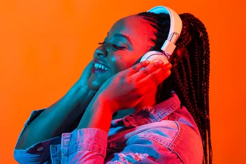 Fotobehang African american young woman listening to music online dancing and singing with headphones, neon light. Music and technology concept. © satura_