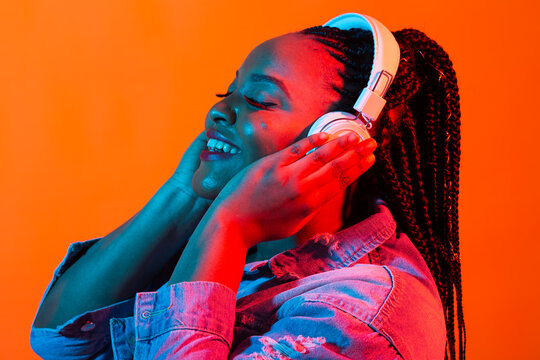 African american young woman listening to music online dancing and singing with headphones, neon light. Music and technology concept.