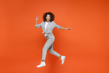 Fototapeta na wymiar Cheerful young african american woman girl in gray casual clothes posing isolated on orange background studio portrait. People lifestyle concept. Mock up copy space. Jumping, spreading hands and legs.