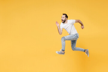 Fototapeta na wymiar Side view of surprised young bearded man guy in white casual t-shirt posing isolated on yellow wall background studio portrait. People lifestyle concept. Mock up copy space. Jumping like running.