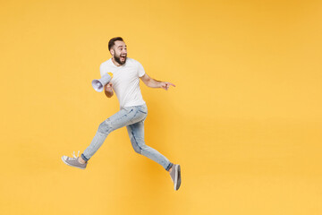 Fototapeta na wymiar Excited young bearded man guy in white casual t-shirt posing isolated on yellow background studio. People lifestyle concept. Mock up copy space. Jumping, hold megaphone, pointing index finger aside.