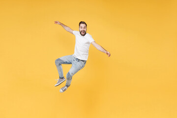 Excited young bearded man guy in white casual t-shirt posing isolated on yellow wall background studio portrait. People sincere emotions lifestyle concept. Mock up copy space. Jumping spreading hands.